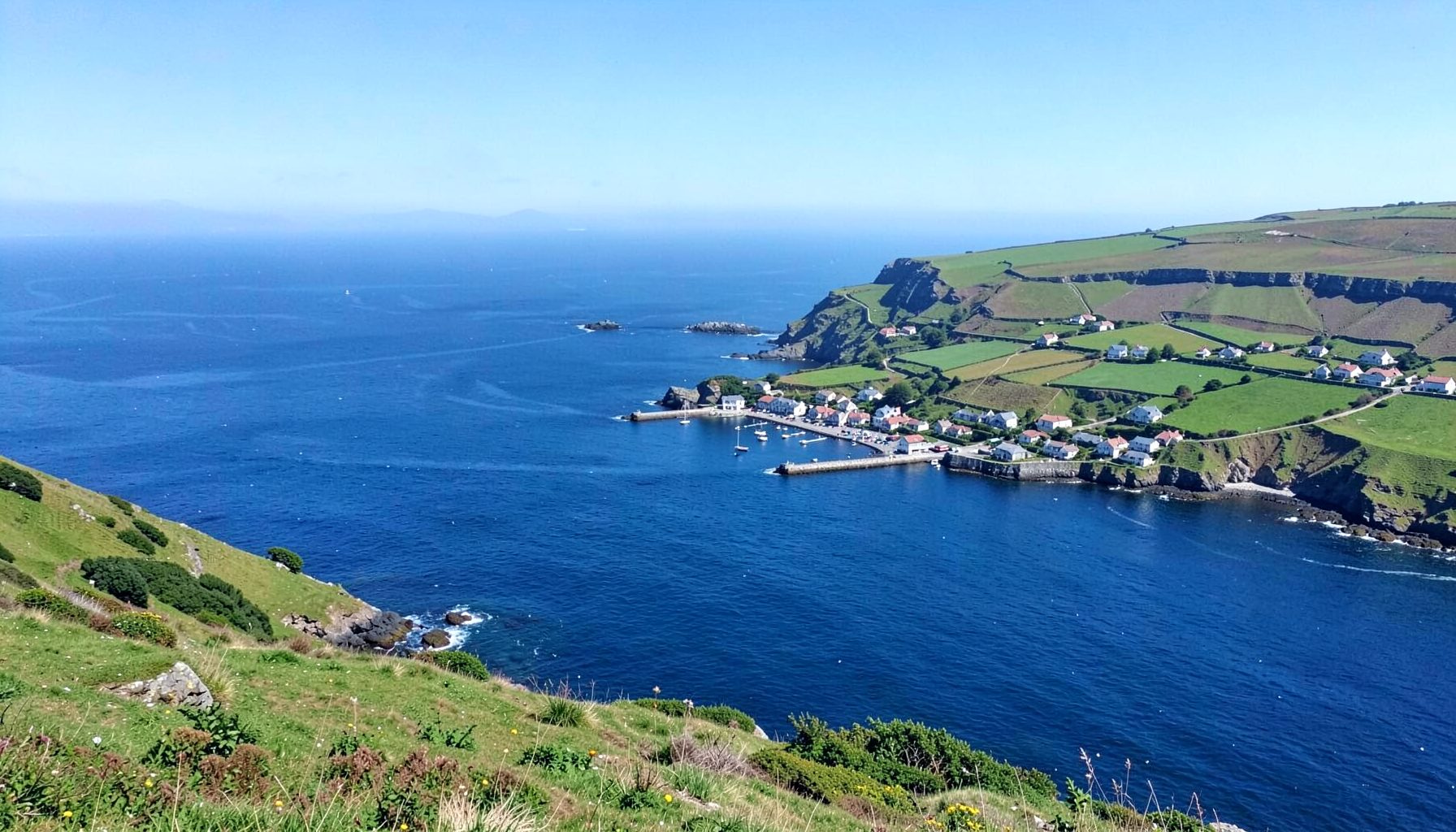A scenic coastal hamlet with a small harbour and green fields sloping down to meet the deep blue Atlantic Ocean
