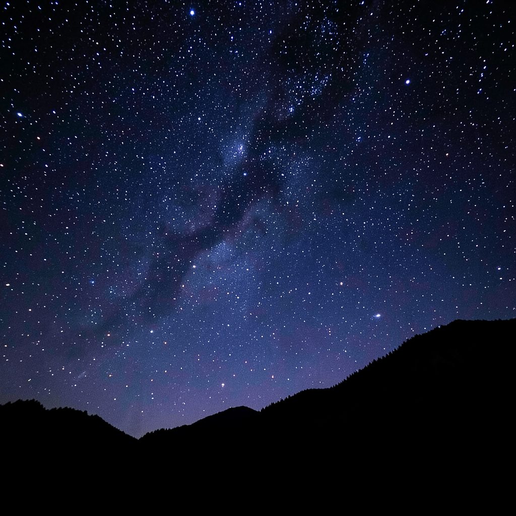 Starry night sky over a silhouetted mountain ridge, deep indigo and black tones with scattered bright stars