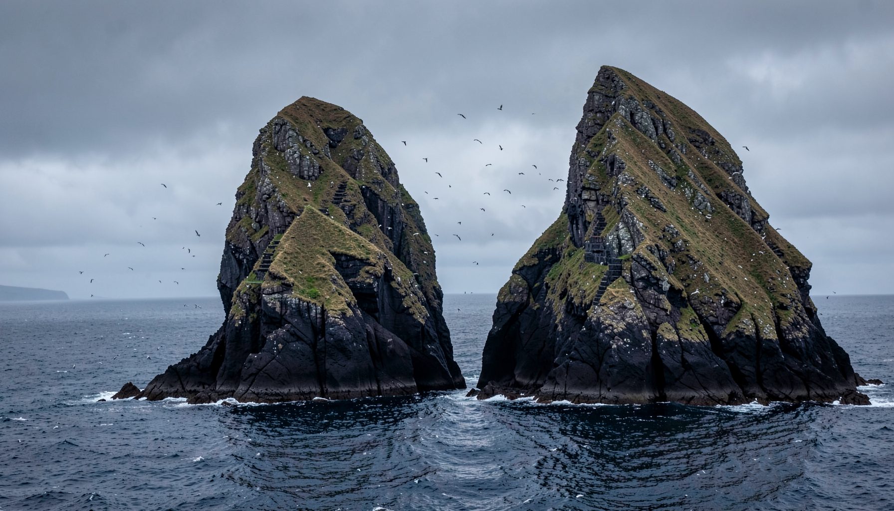 Dramatic twin peaks of Skellig Michael rising from the Atlantic Ocean under a moody grey sky, with seabirds circling the ancient stone steps carved into the steep rock face